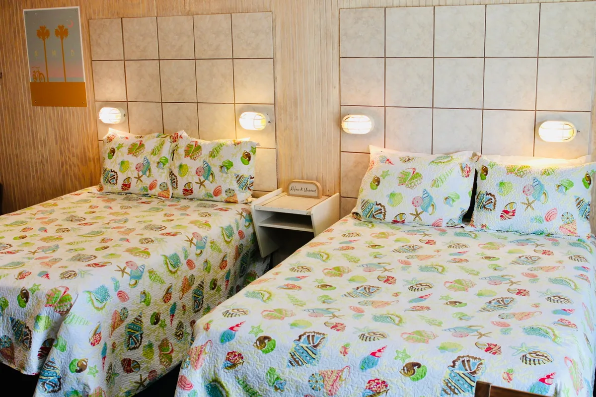 The scene shows two beds with vibrant quilts, unique wall lamps, and decorative wall art. The atmosphere is cheerful and cozy, ideal for families or groups to gather, relax, and share stories. The setup captures both relaxation and socialization, making it appealing for guests wanting to unwind together.