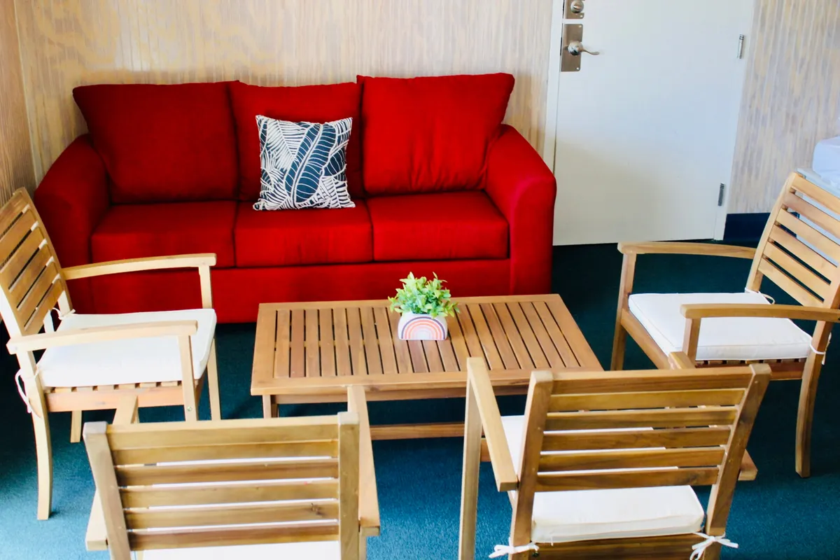 Featuring a red sofa, wooden coffee table, green plant, and a decorative pillow, this cozy corner invites guests to gather for casual conversations, reading, or simply relaxing. The natural textures and warm tones make the space feel welcoming and homey—perfect for downtime with family, friends, or pets.
