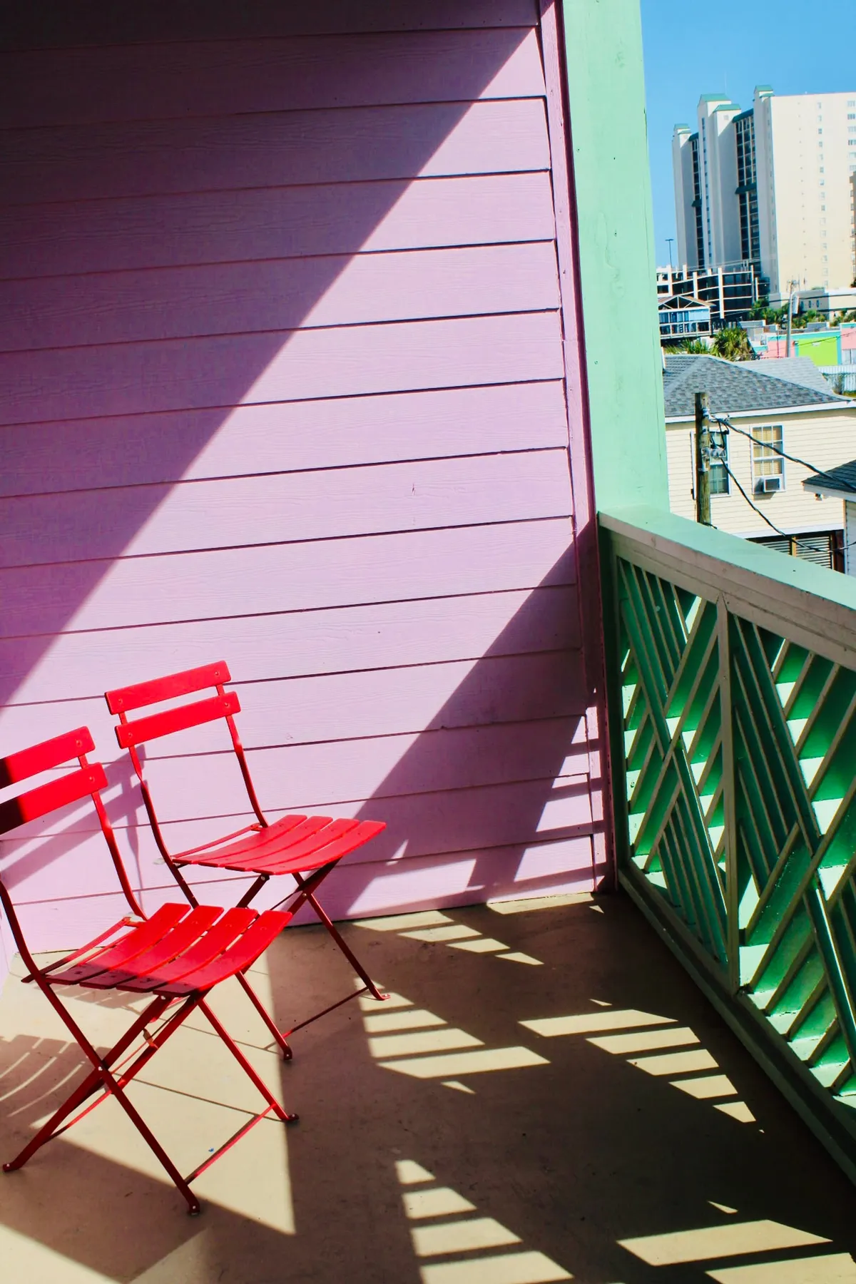 The image showcases the studio's inviting exterior with vibrant red bistro chairs set against a colorful wall and decorative railing, hinting at a cozy spot to relax. The setting is ideal for enjoying sunrise coffee, sunset views, or lively outdoor meals just steps from the ocean.